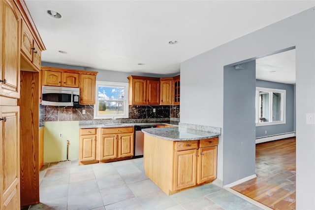 kitchen with backsplash, sink, baseboard heating, light stone counters, and stainless steel appliances