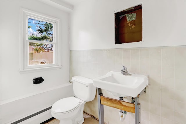 bathroom with sink, toilet, baseboard heating, and tile walls