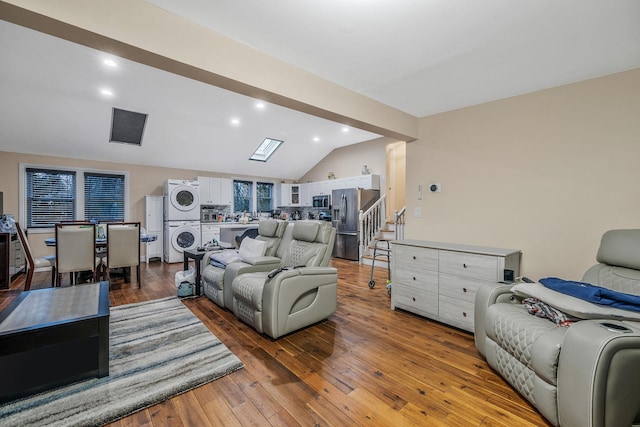 living room featuring lofted ceiling with skylight, stacked washer and dryer, and light wood-type flooring