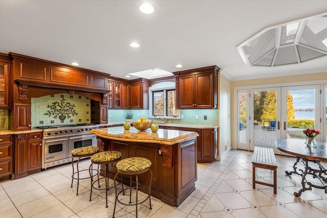 kitchen with french doors, backsplash, light tile patterned floors, range with two ovens, and a center island