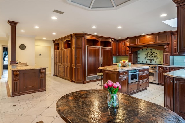 kitchen featuring decorative backsplash, light stone countertops, premium appliances, a kitchen island, and decorative columns