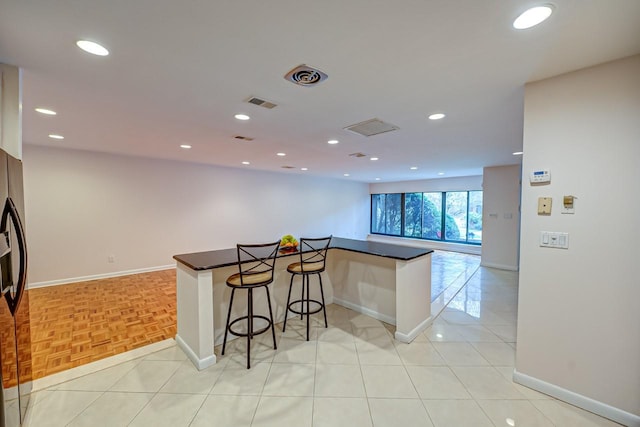 kitchen featuring a kitchen bar, kitchen peninsula, stainless steel refrigerator, and light parquet floors