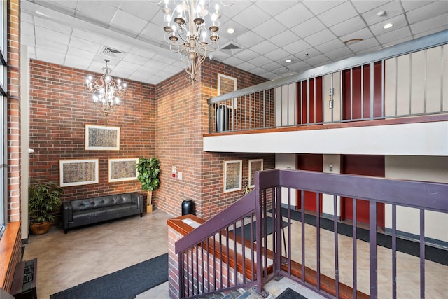 interior space with a drop ceiling, a towering ceiling, a chandelier, and brick wall