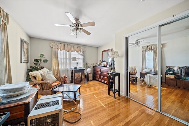 living area with ceiling fan, heating unit, and light hardwood / wood-style flooring