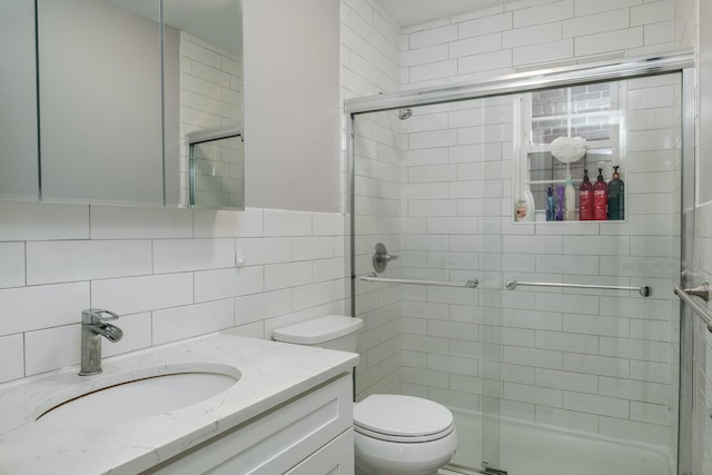 bathroom with backsplash, vanity, tile walls, toilet, and a shower with shower door