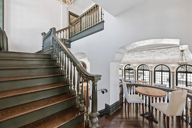 stairway featuring arched walkways, a high ceiling, wood finished floors, baseboards, and an inviting chandelier