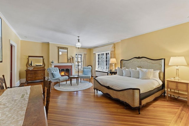 bedroom featuring a warm lit fireplace, baseboards, wood finished floors, and ornamental molding