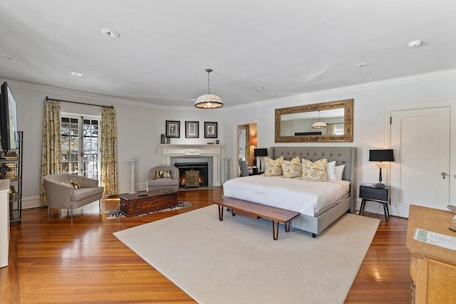 bedroom featuring a warm lit fireplace, ornamental molding, wood finished floors, and baseboards