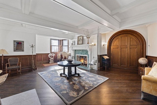 living room featuring dark wood-type flooring, beam ceiling, wainscoting, and a fireplace