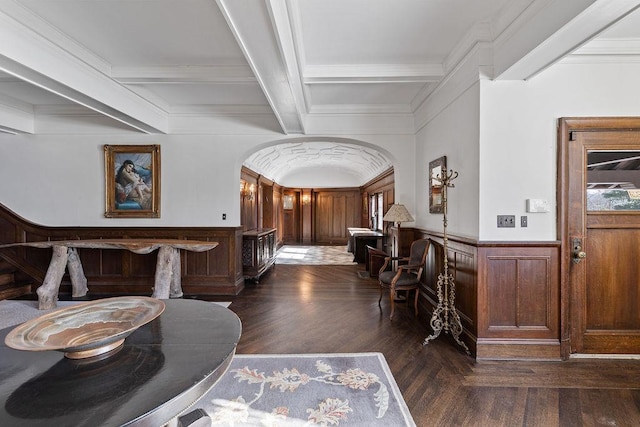 entrance foyer with dark wood-type flooring, arched walkways, a wainscoted wall, and beamed ceiling