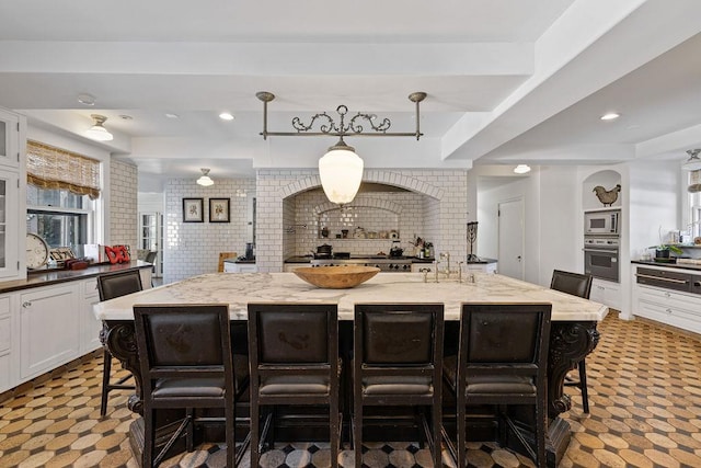 kitchen featuring a center island with sink, stainless steel appliances, white cabinetry, light stone countertops, and a kitchen bar