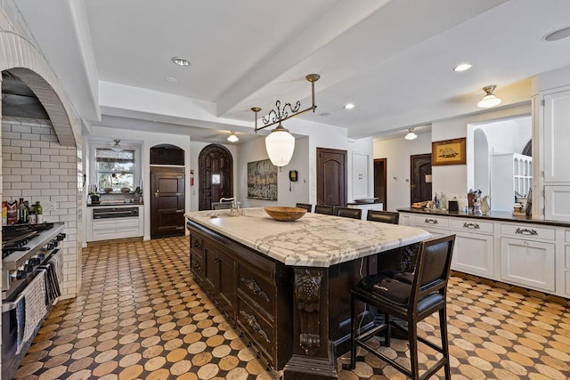 kitchen featuring arched walkways, white cabinetry, an island with sink, a kitchen bar, and decorative light fixtures