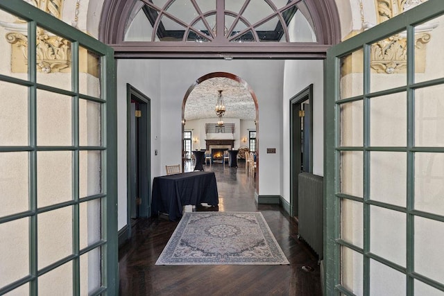 foyer entrance with a warm lit fireplace, high vaulted ceiling, arched walkways, baseboards, and dark wood-style floors