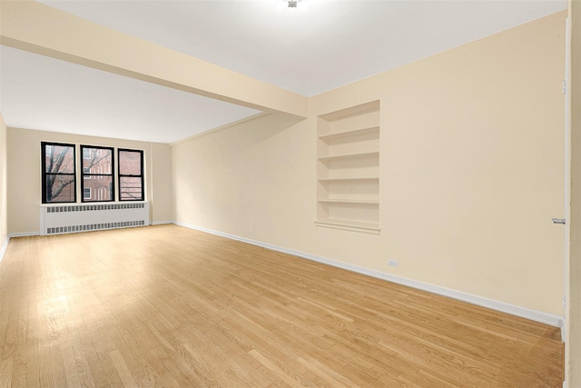 spare room with built in shelves, radiator heating unit, and light hardwood / wood-style floors