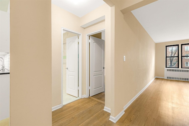 corridor with radiator heating unit, light hardwood / wood-style floors, and lofted ceiling