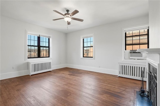 spare room with a fireplace, radiator, dark wood-type flooring, and ceiling fan