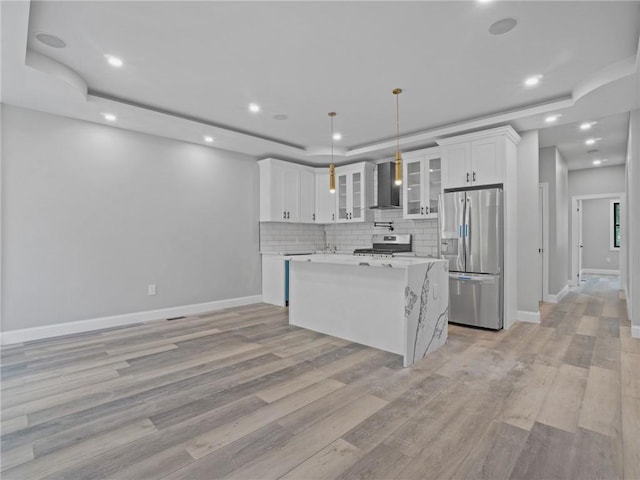 kitchen with appliances with stainless steel finishes, white cabinetry, hanging light fixtures, and wall chimney exhaust hood