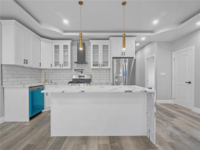 kitchen with white cabinets, wall chimney exhaust hood, stainless steel appliances, and hanging light fixtures