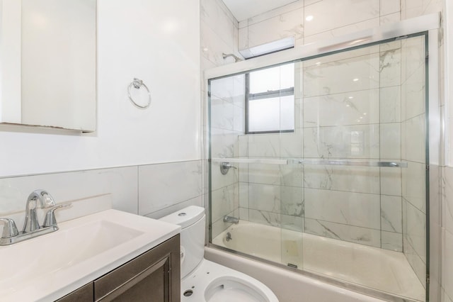 full bathroom featuring combined bath / shower with glass door, vanity, toilet, and tile walls