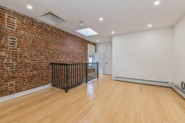 spare room featuring a skylight, brick wall, light wood-type flooring, and a baseboard heating unit