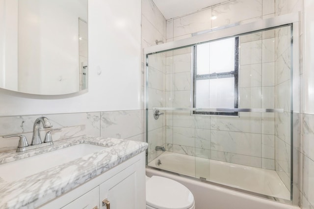 full bathroom featuring combined bath / shower with glass door, vanity, toilet, and tile walls