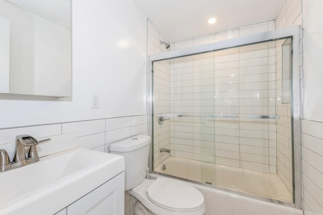 full bathroom with toilet, vanity, tile walls, and combined bath / shower with glass door