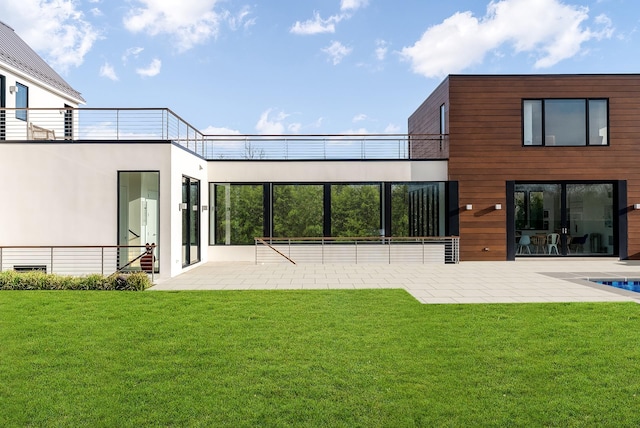 rear view of property with a balcony, a patio area, and a lawn