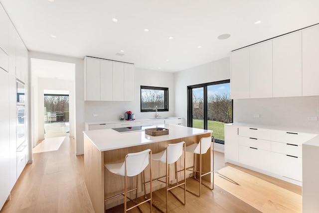 kitchen with light hardwood / wood-style floors, a kitchen breakfast bar, a kitchen island, and white cabinetry