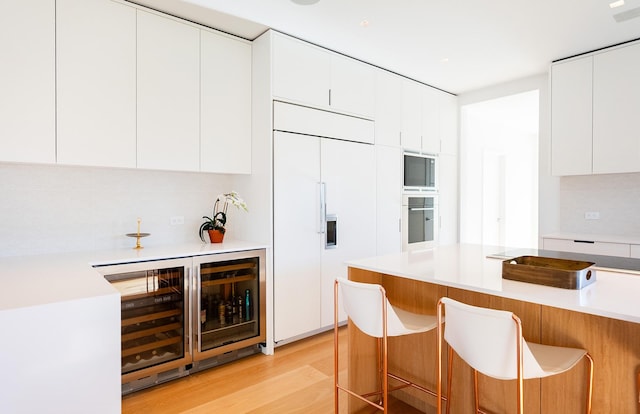 kitchen featuring wine cooler, light wood-type flooring, paneled fridge, a kitchen bar, and white cabinetry