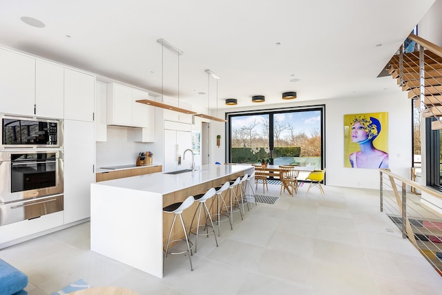 kitchen with pendant lighting, white cabinets, a center island with sink, sink, and built in appliances