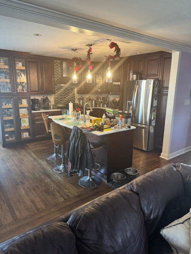 kitchen with a kitchen island with sink, crown molding, hanging light fixtures, a kitchen bar, and stainless steel fridge with ice dispenser