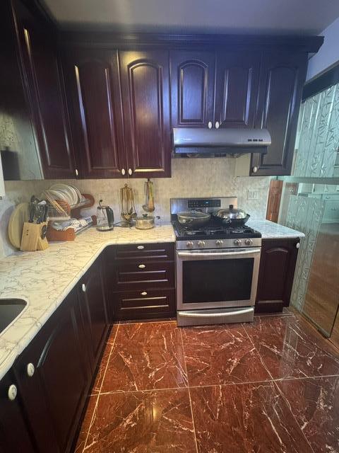 kitchen featuring light stone counters, backsplash, and gas range