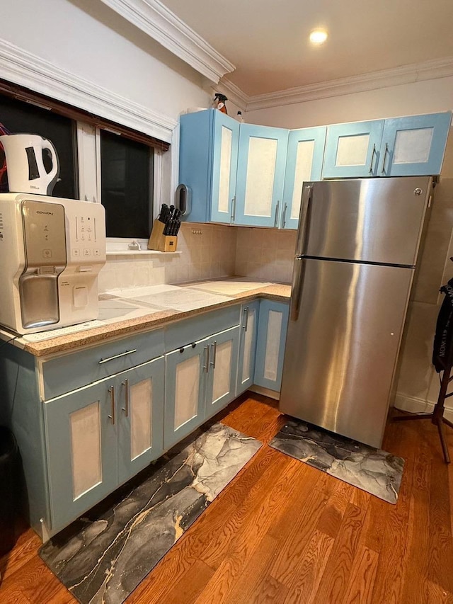 kitchen with stainless steel refrigerator, blue cabinetry, ornamental molding, dark wood-type flooring, and tasteful backsplash