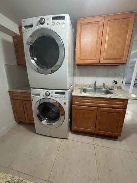 clothes washing area with sink, stacked washer / drying machine, light tile patterned flooring, and cabinets