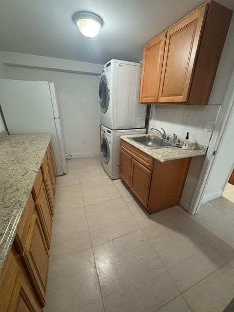 clothes washing area featuring sink, stacked washer and clothes dryer, and cabinets