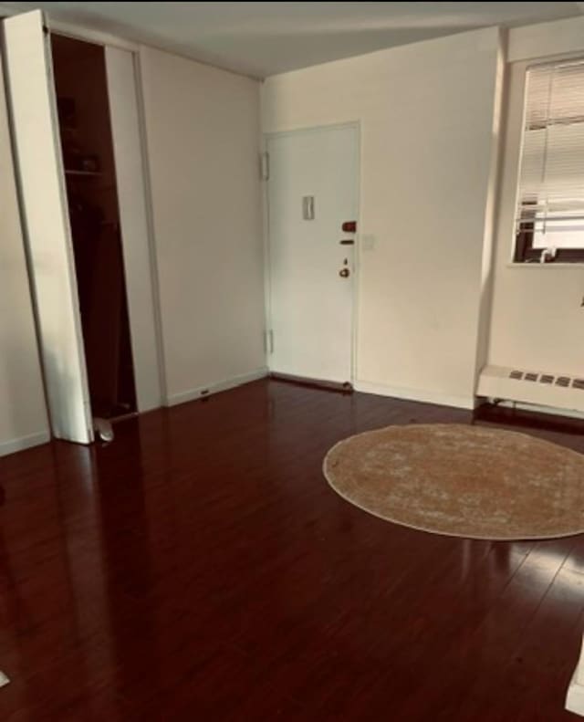 unfurnished room featuring baseboard heating and dark wood-type flooring