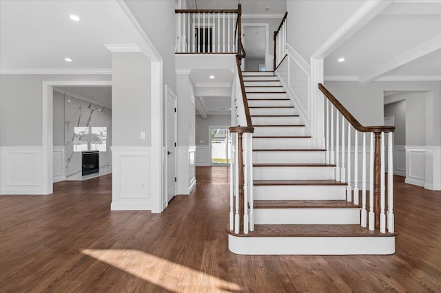 staircase featuring a high end fireplace, wood-type flooring, and ornamental molding