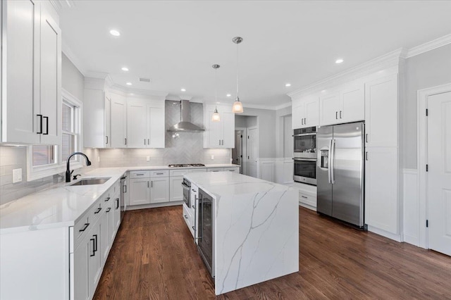 kitchen featuring wall chimney exhaust hood, stainless steel appliances, sink, pendant lighting, and a kitchen island