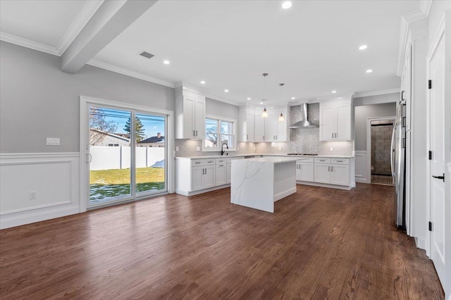 kitchen featuring white cabinets, a center island, wall chimney exhaust hood, and pendant lighting