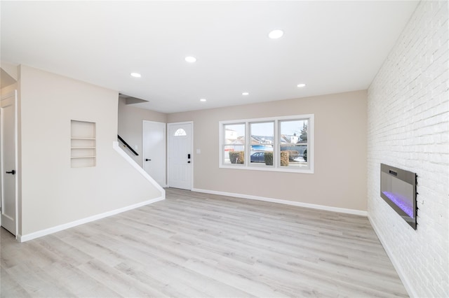 unfurnished living room featuring built in features, light wood-type flooring, a fireplace, and brick wall