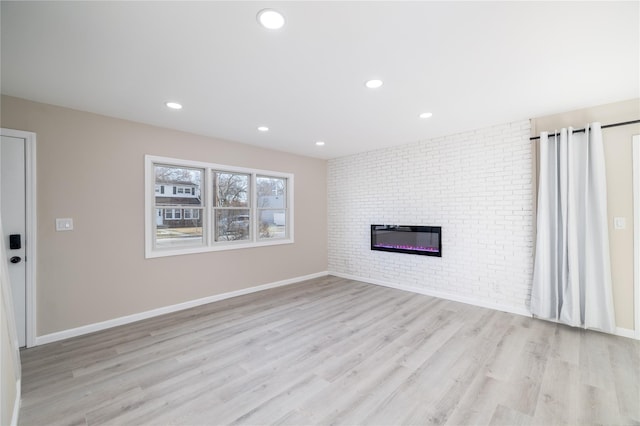 unfurnished living room featuring a brick fireplace, light hardwood / wood-style flooring, and brick wall