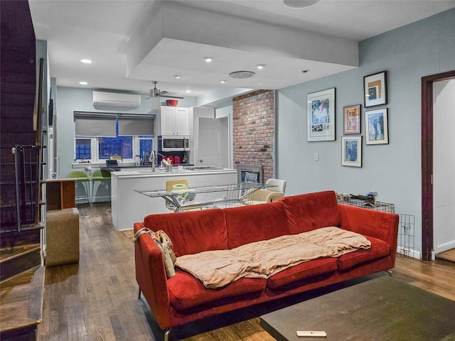 living room with ceiling fan, a fireplace, a wall unit AC, and hardwood / wood-style flooring