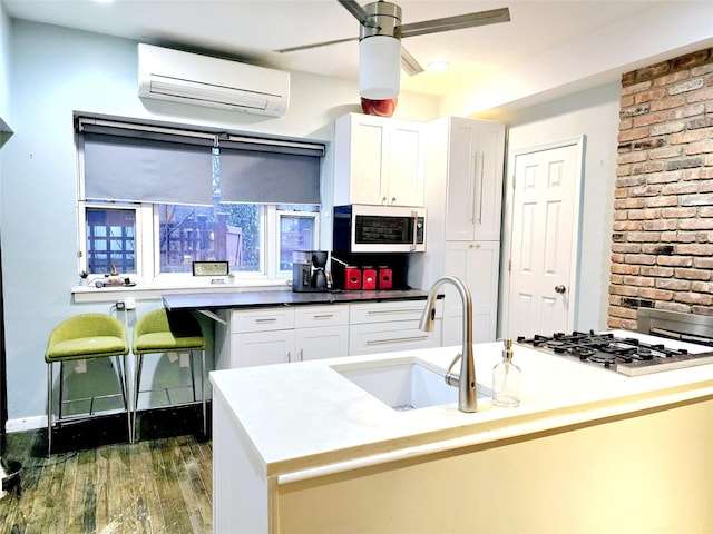 kitchen featuring sink, stainless steel gas stovetop, white cabinetry, and an AC wall unit