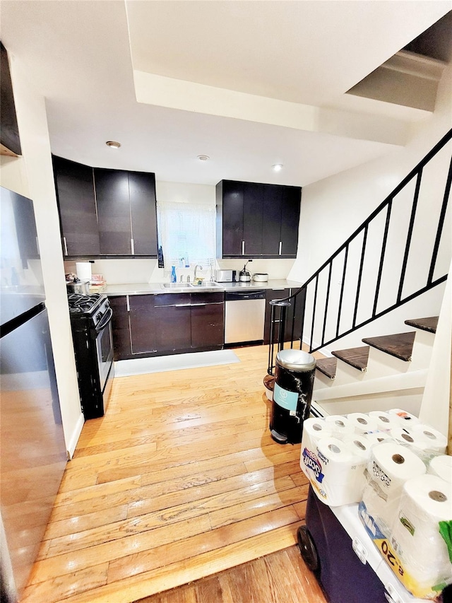 kitchen with stainless steel dishwasher, sink, gas stove, and light hardwood / wood-style flooring