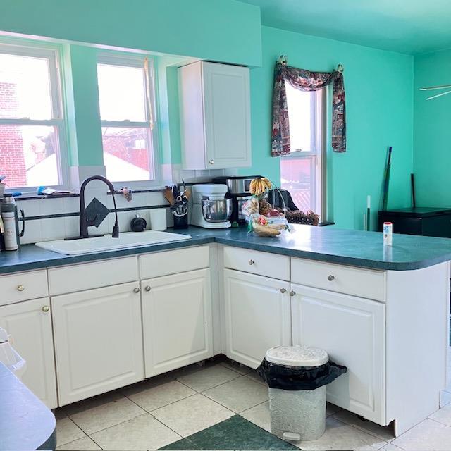 kitchen with light tile patterned flooring, kitchen peninsula, white cabinetry, and sink