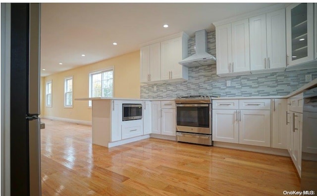 kitchen with wall chimney exhaust hood, stainless steel appliances, kitchen peninsula, decorative backsplash, and white cabinets