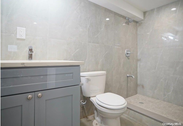 bathroom with vanity, toilet, tile walls, and a tile shower