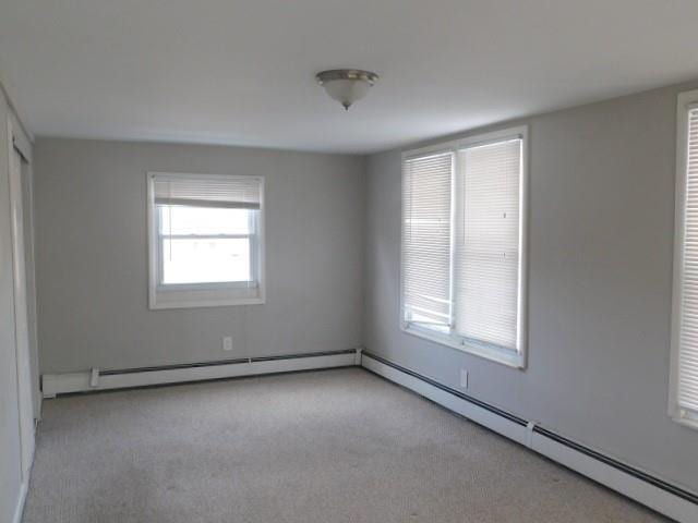 unfurnished room featuring light carpet and a baseboard heating unit