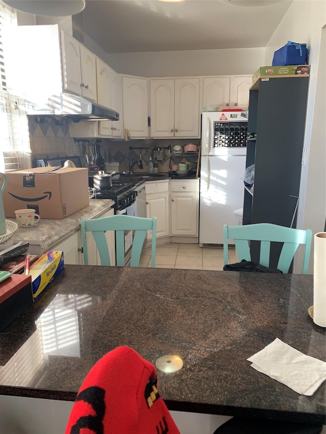 kitchen with range with gas stovetop, white refrigerator, white cabinetry, and light tile patterned floors