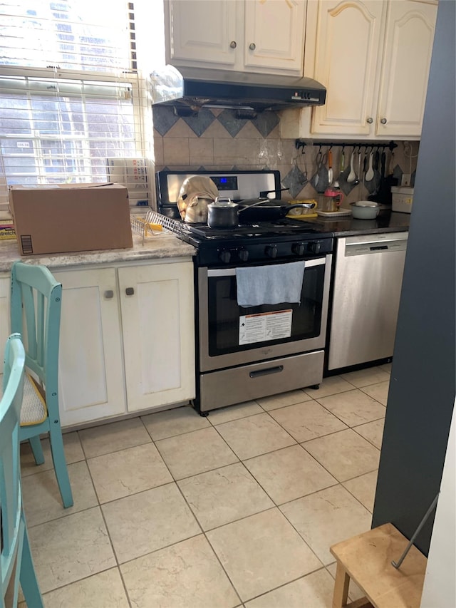 kitchen with light tile patterned flooring, backsplash, stainless steel appliances, white cabinetry, and range hood